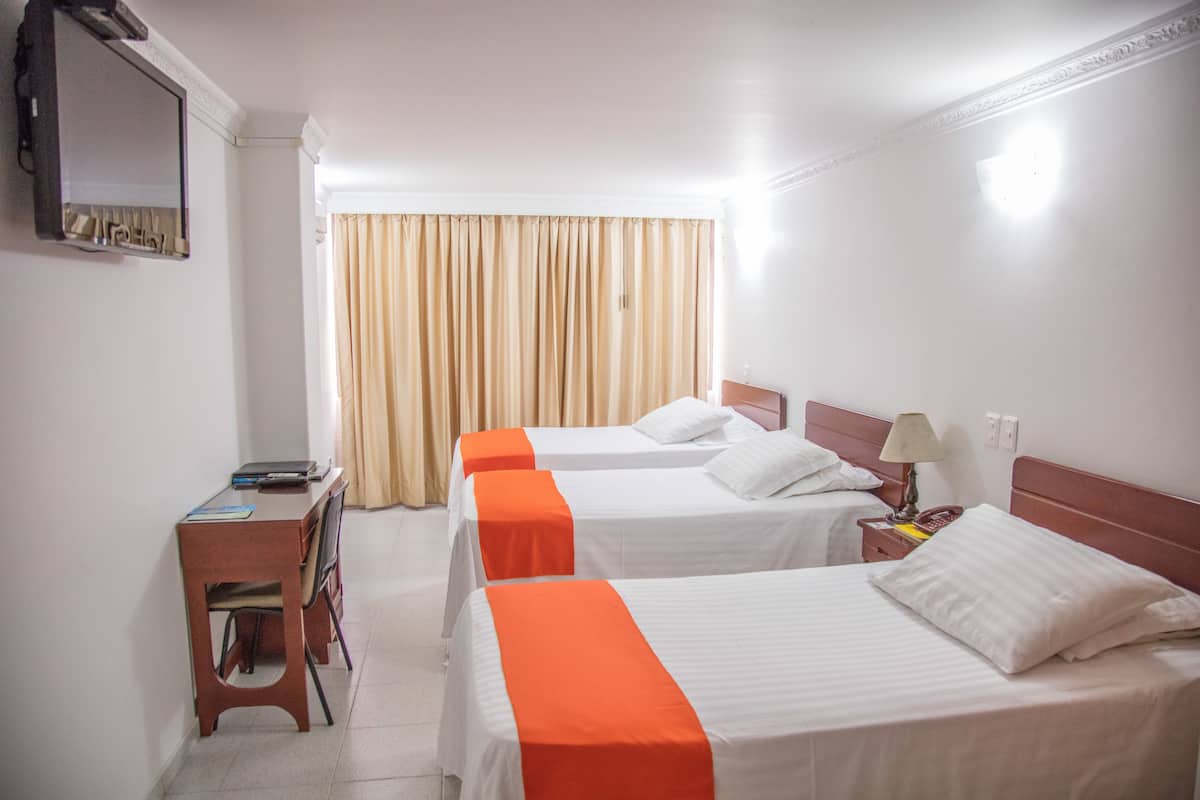 A hotel room with two single beds, a desk with a chair, a mirror, and a window with curtains.