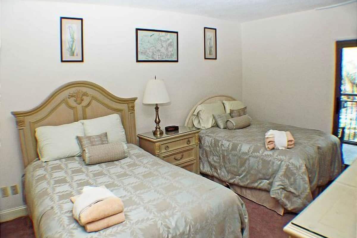 Una habitación de hotel con dos camas, una mesita de noche con lámpara y cuadros en la pared.