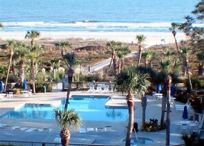 A pool area with palm trees and a view of the ocean. - Forest Beach by Seashore Vacations (Hilton Head Island)