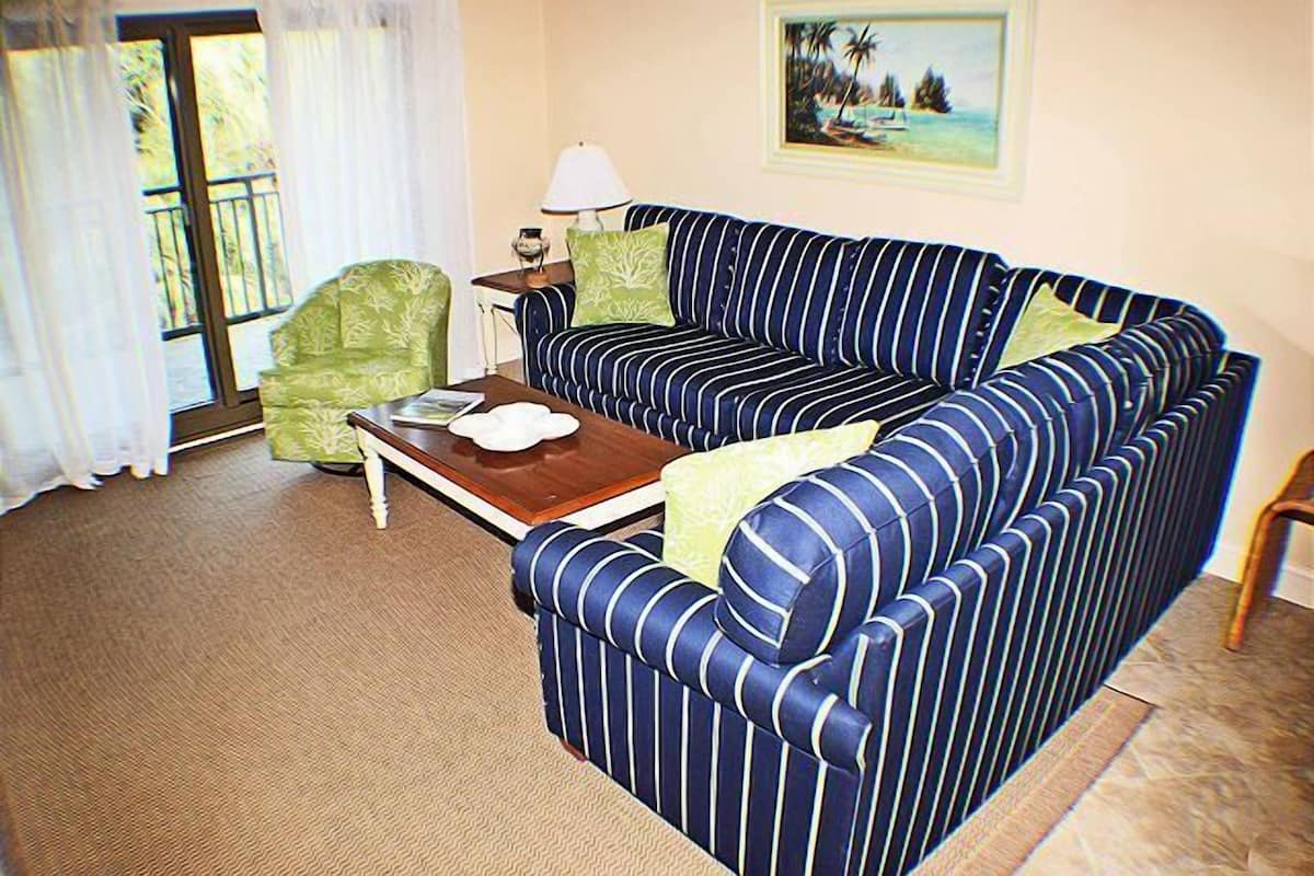 Una sala de estar con un sofá a rayas, un sillón verde, una mesa de centro de madera y una lámpara.