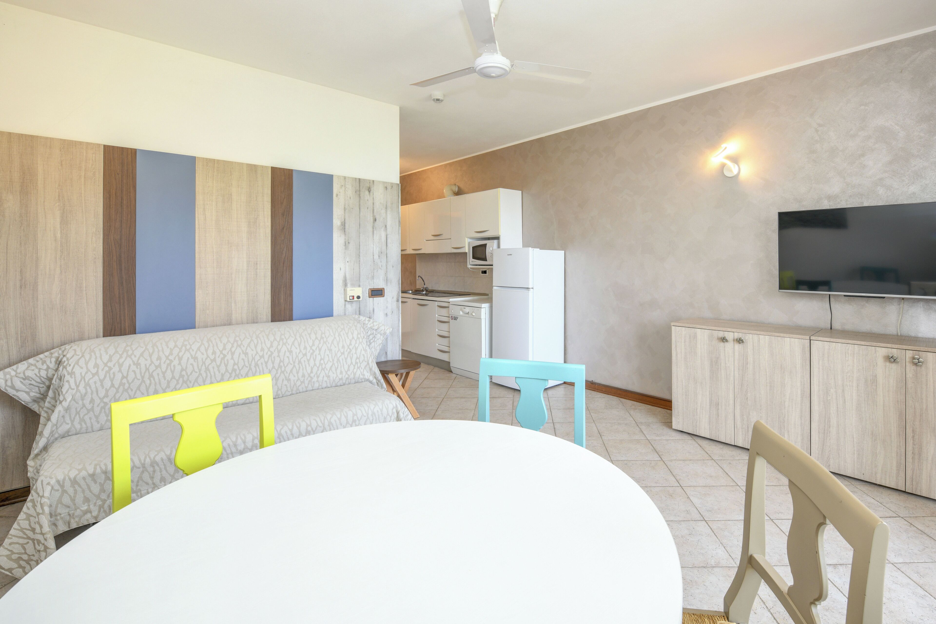 A modern hotel room with a bed, a dining table, and a kitchenette.