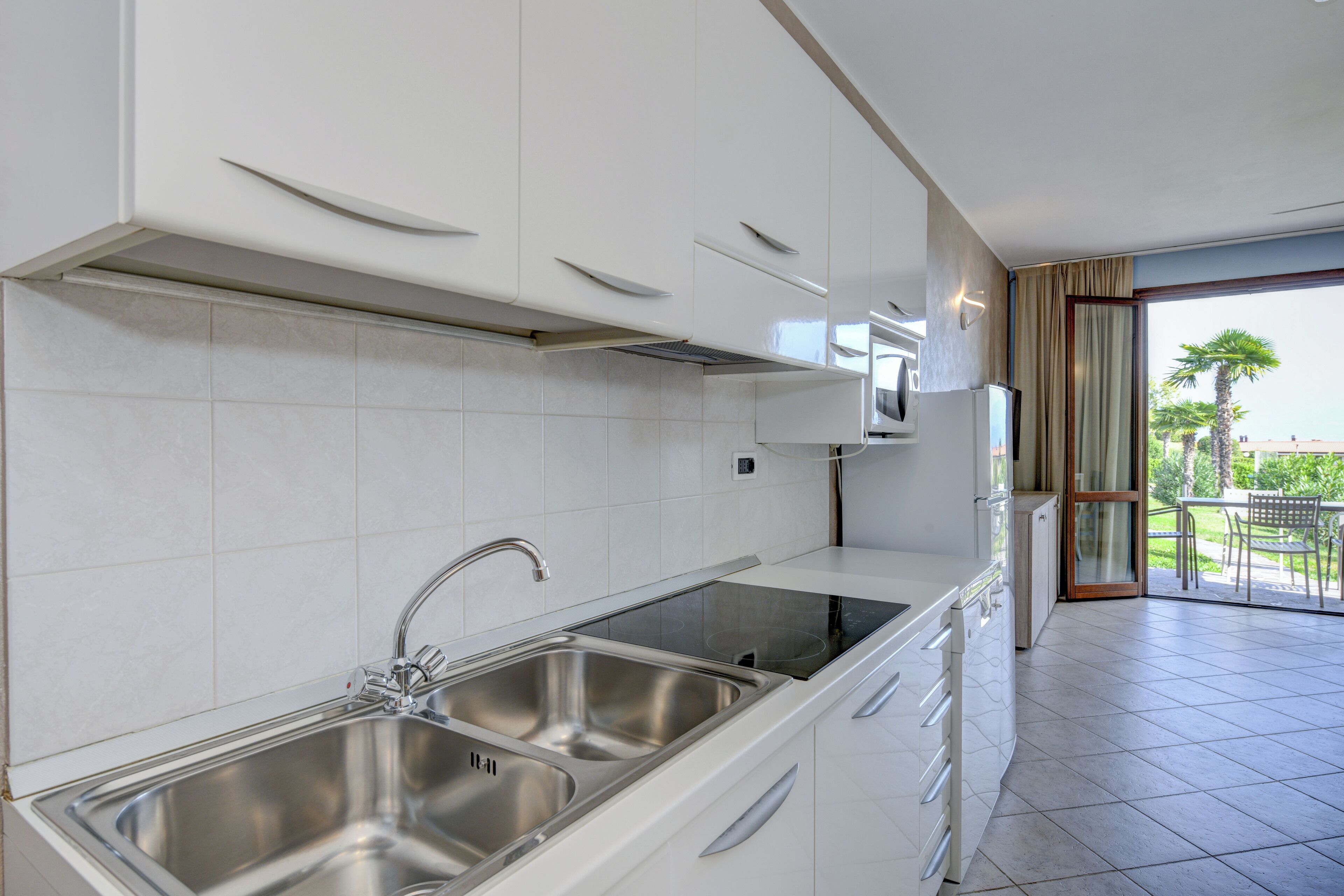 A modern kitchen with a double sink, white cabinets, and a view of the outdoor balcony.
