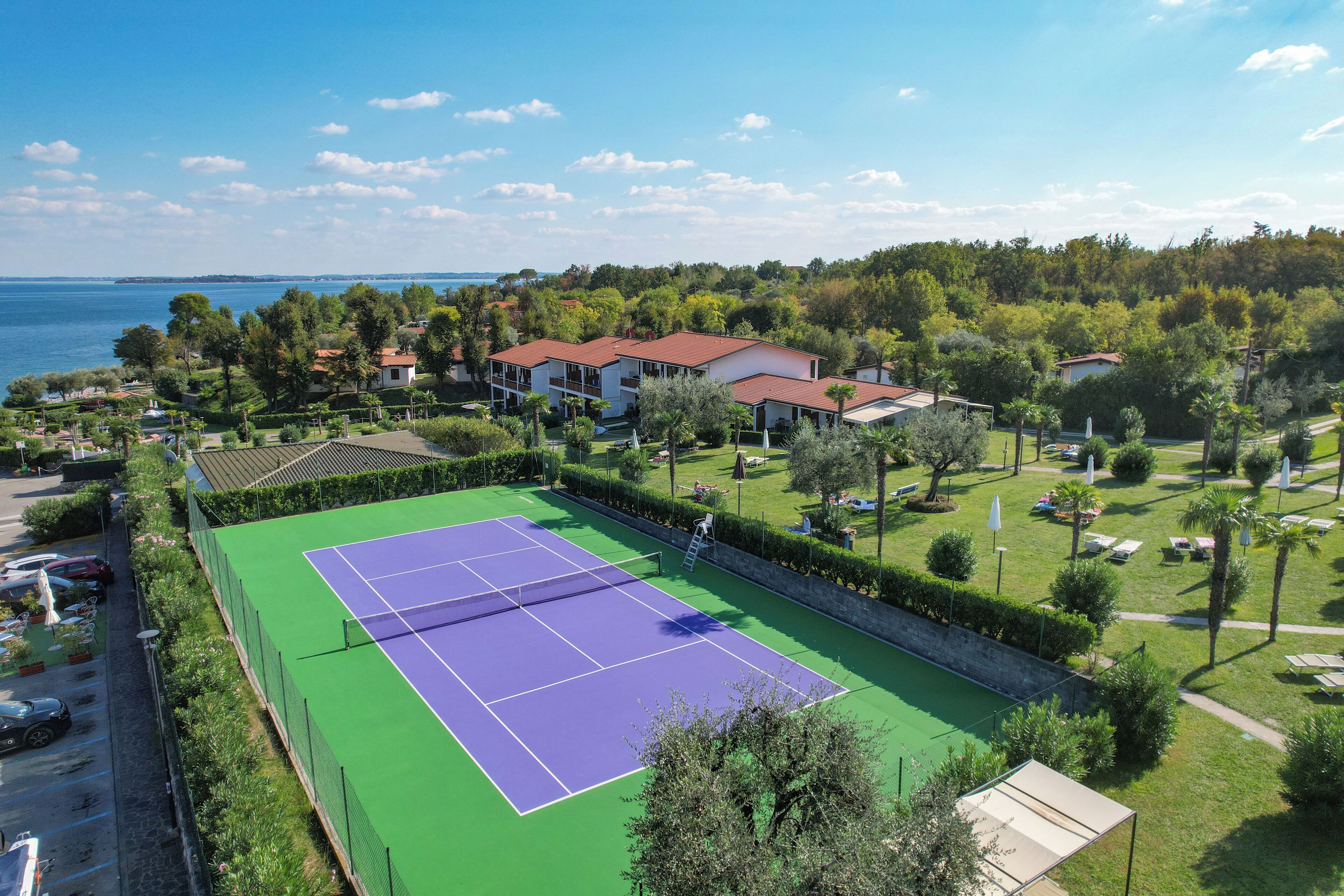 Una cancha de tenis rodeada de exuberante vegetación y casas.