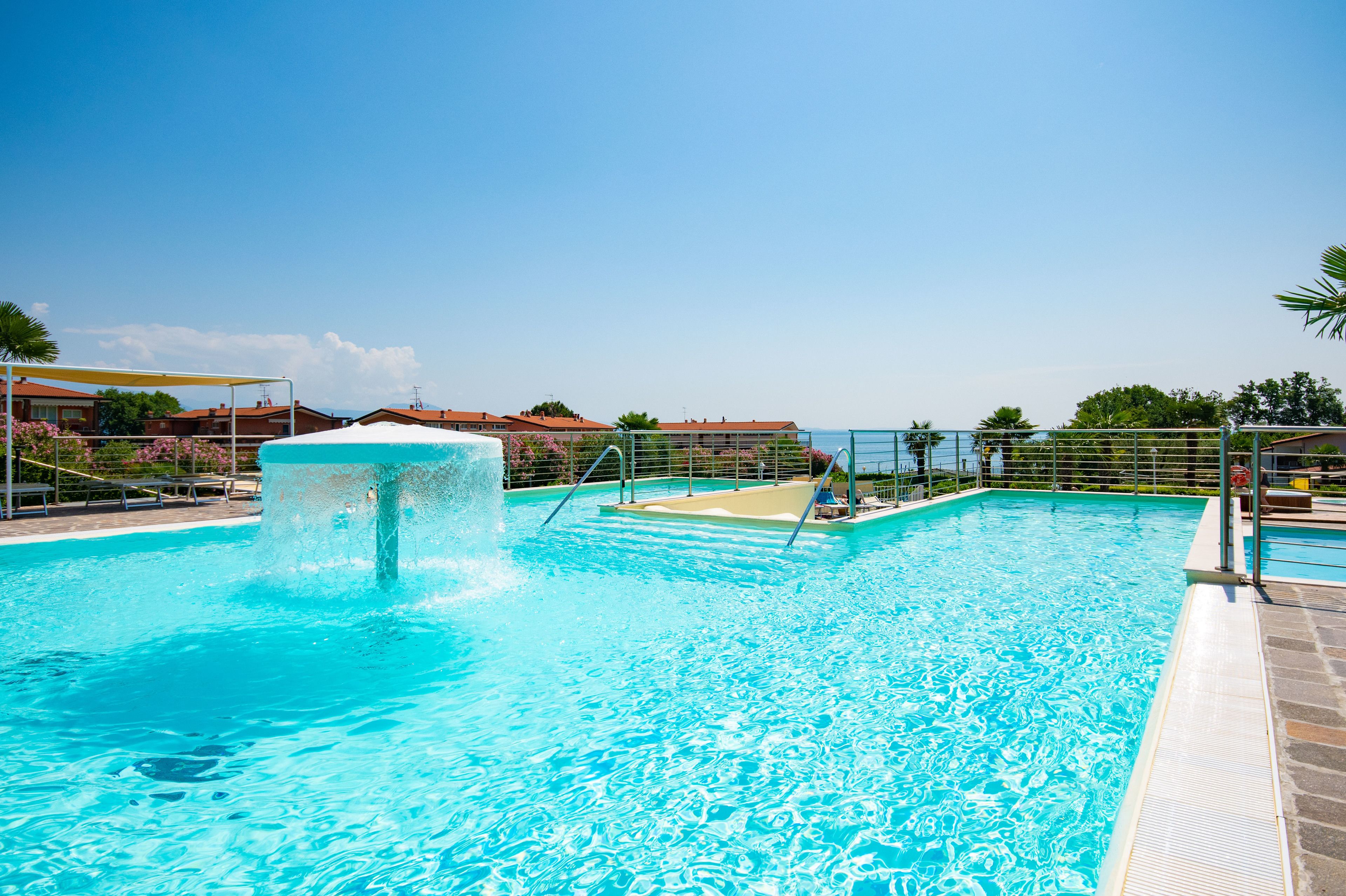 A swimming pool with a water fountain, surrounded by a fence and a clear sky.