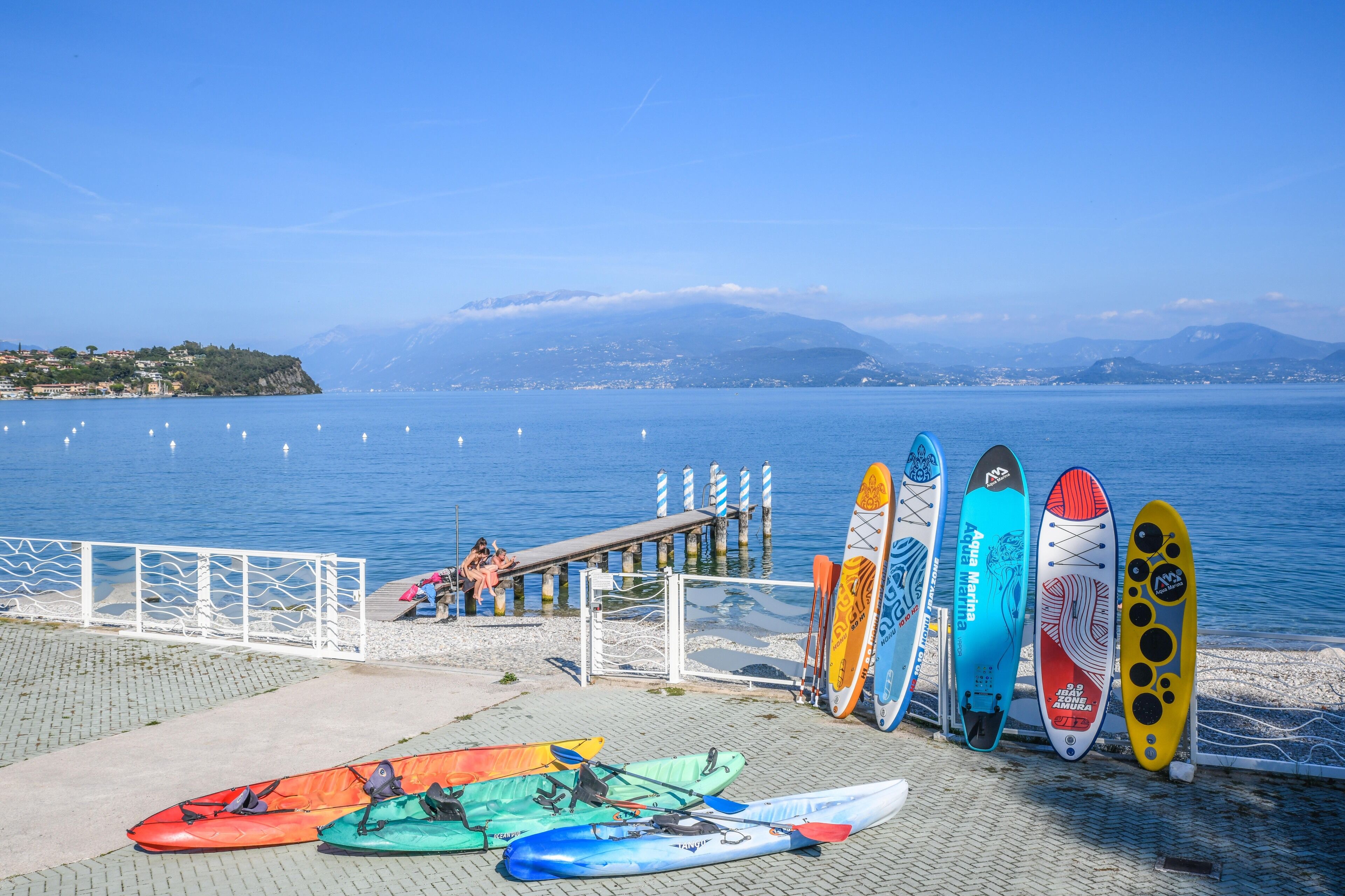 A waterfront with kayaks and paddleboards lined up on a dock.