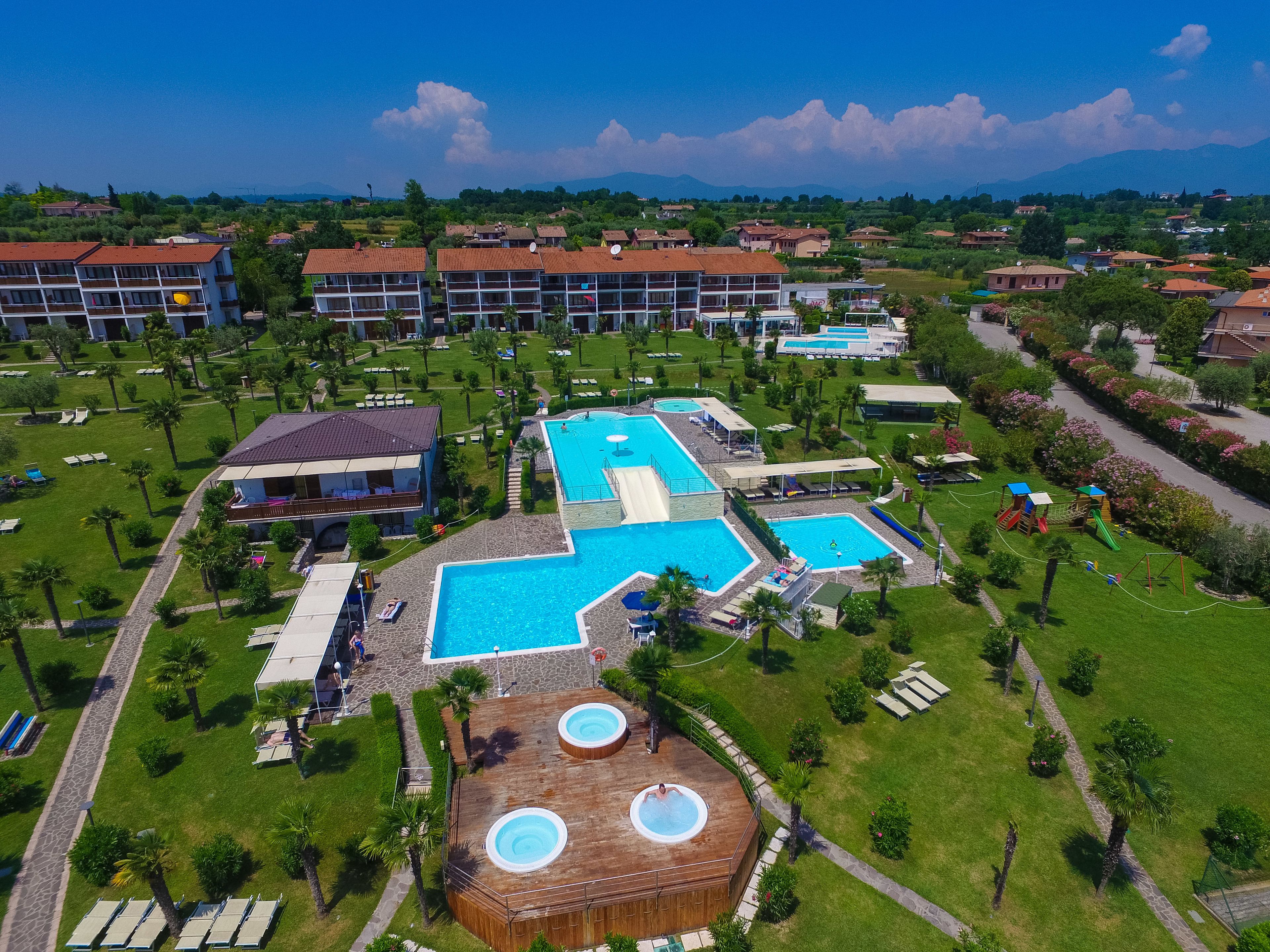 Een resort met meerdere zwembaden, een houten terras met een jacuzzi en een weelderig groen landschap.