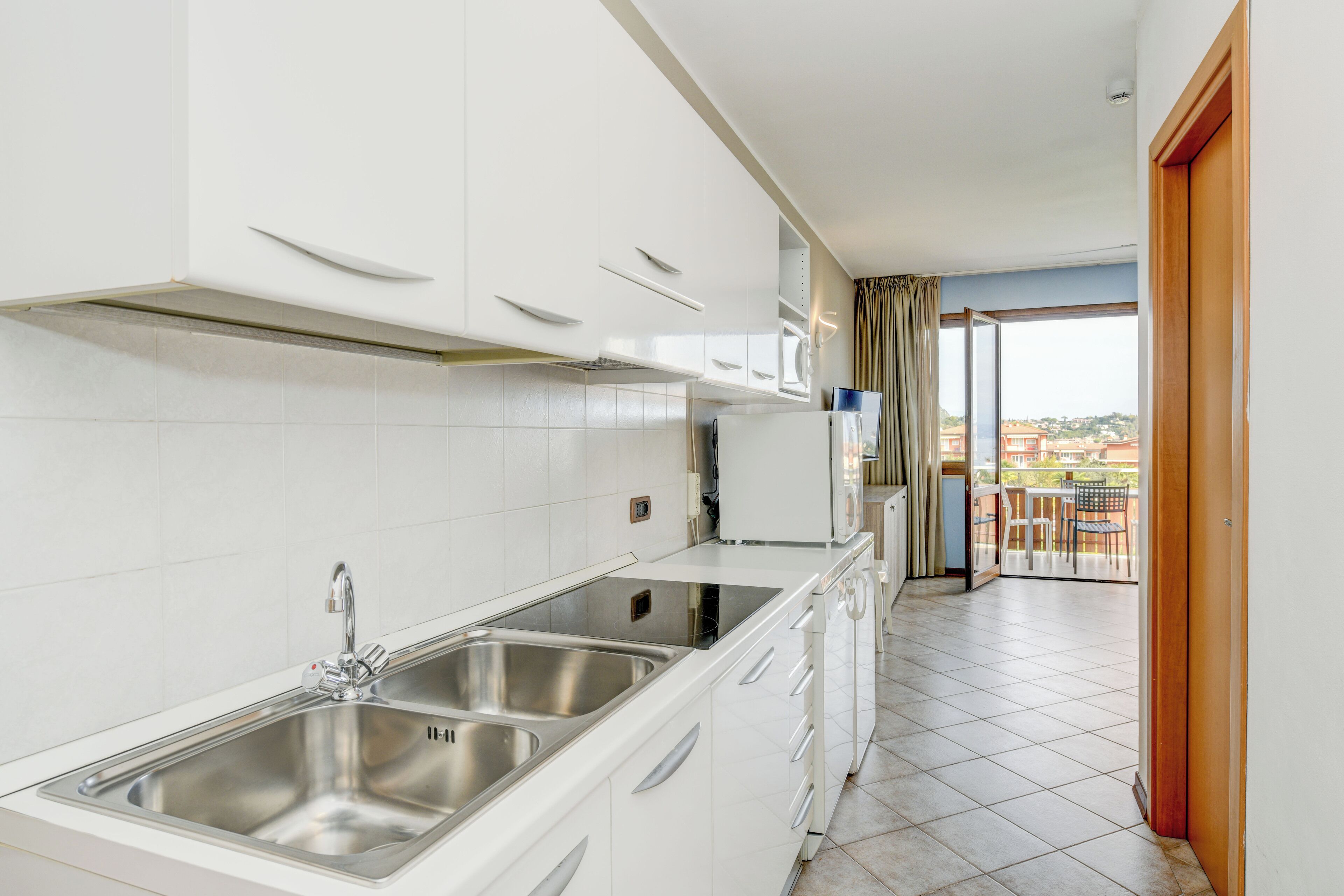 Eine moderne Küche mit weißen Schränken, einer doppelten Spüle und Blick auf einen Balkon mit Sitzmöbeln.