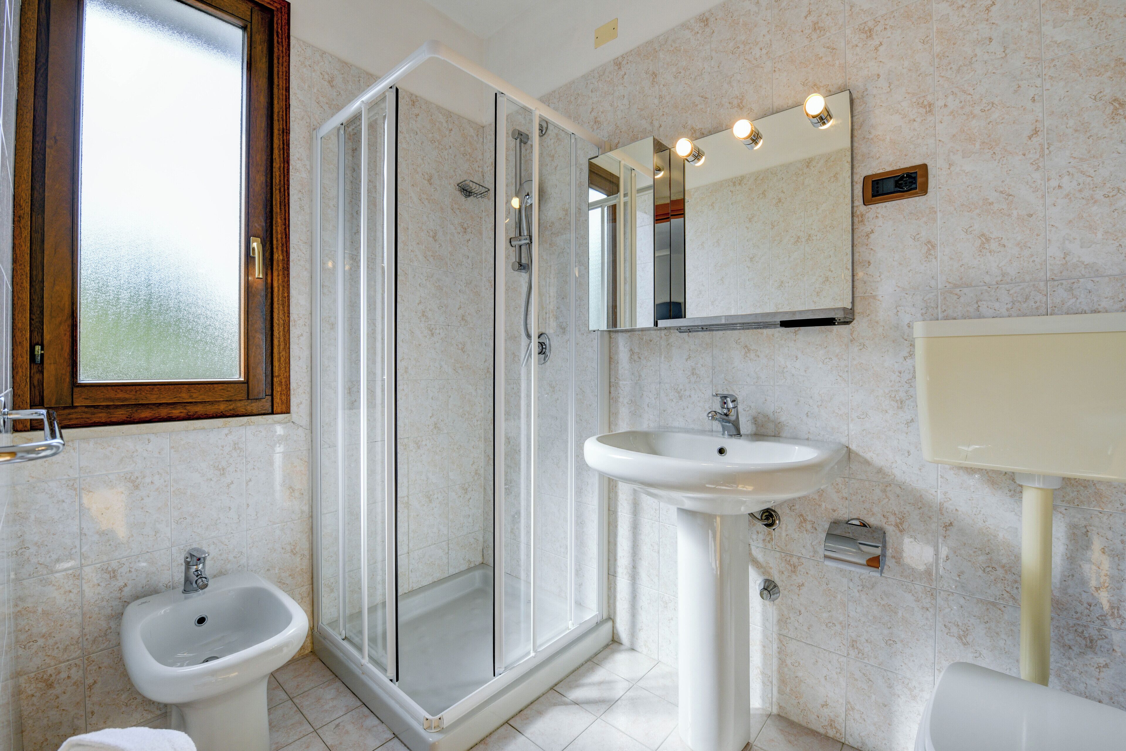 A bathroom with a glass-enclosed shower, a pedestal sink, and a toilet.