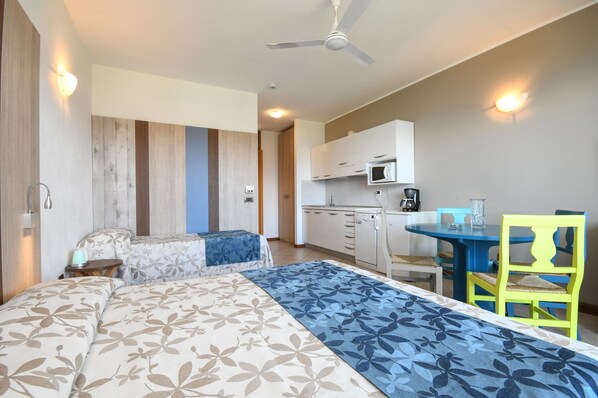 A bedroom with two beds, a kitchenette, a dining area, and a ceiling fan. - Apparthotel San Sivino (Manerba del Garda)