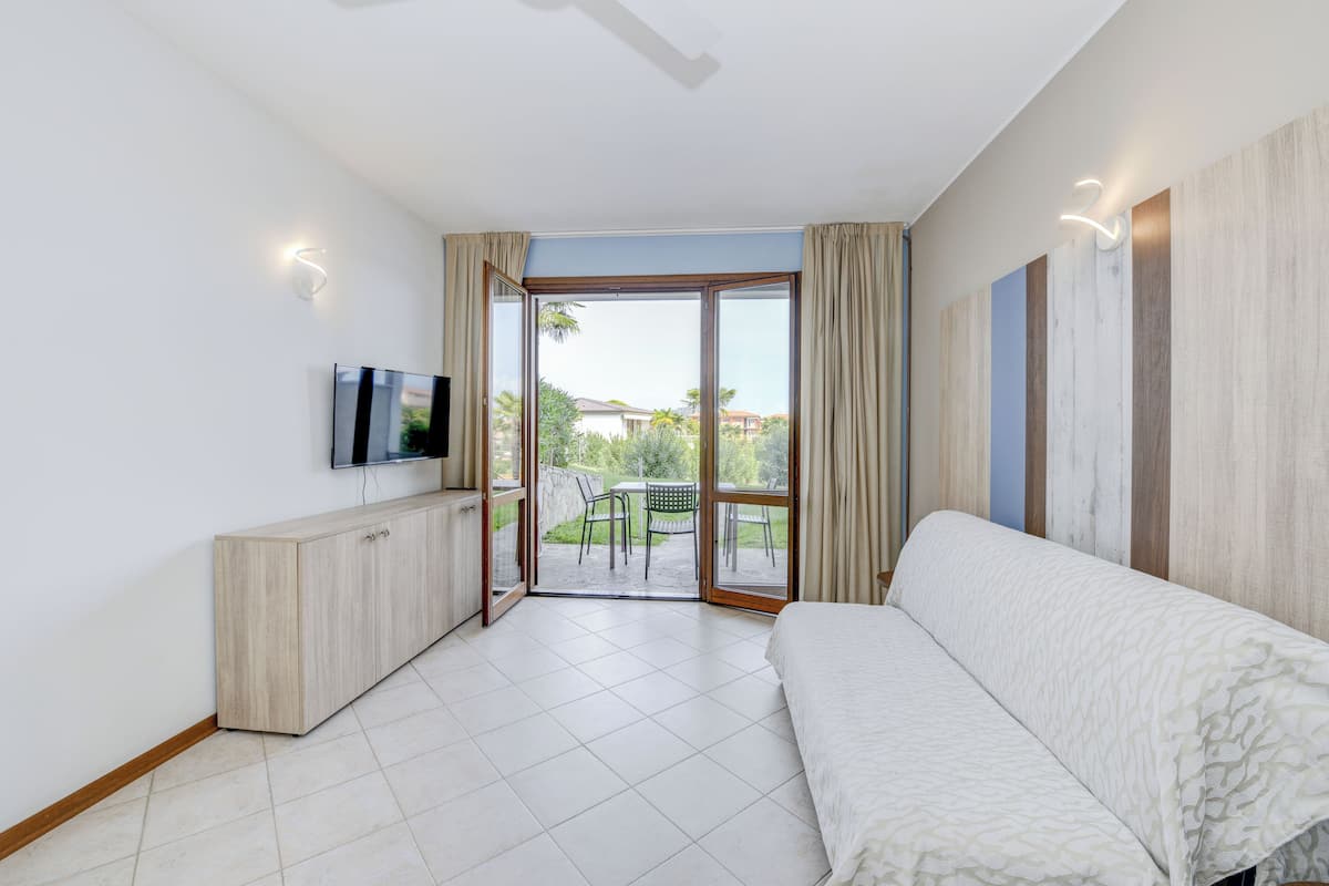 A modern hotel room with a large window, a sofa, a TV, and a wooden cabinet.