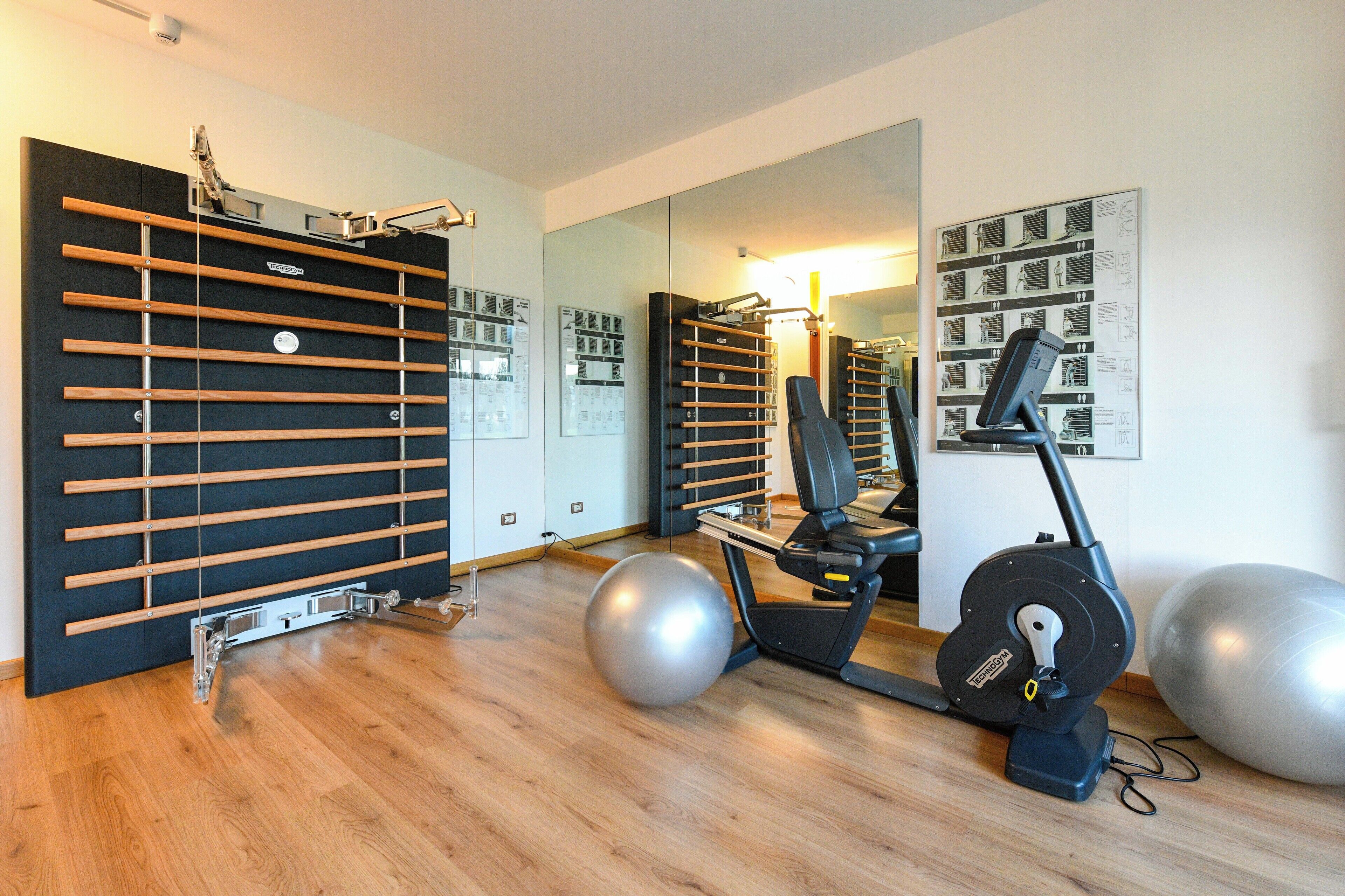 A gym with exercise equipment, a mirrored wall, and wooden flooring.