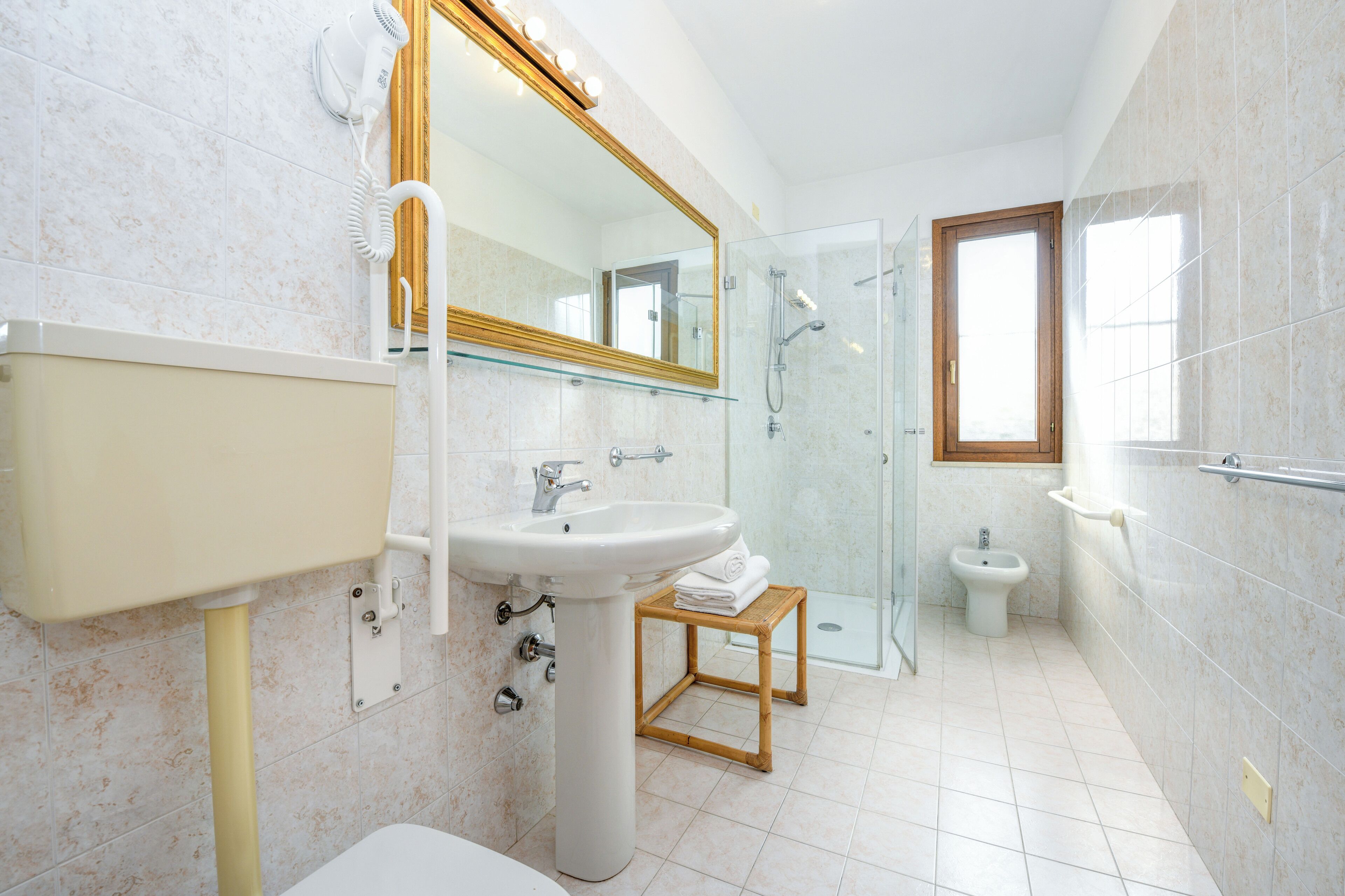 A modern bathroom with a pedestal sink, a glass shower enclosure, and a vanity with a mirror.