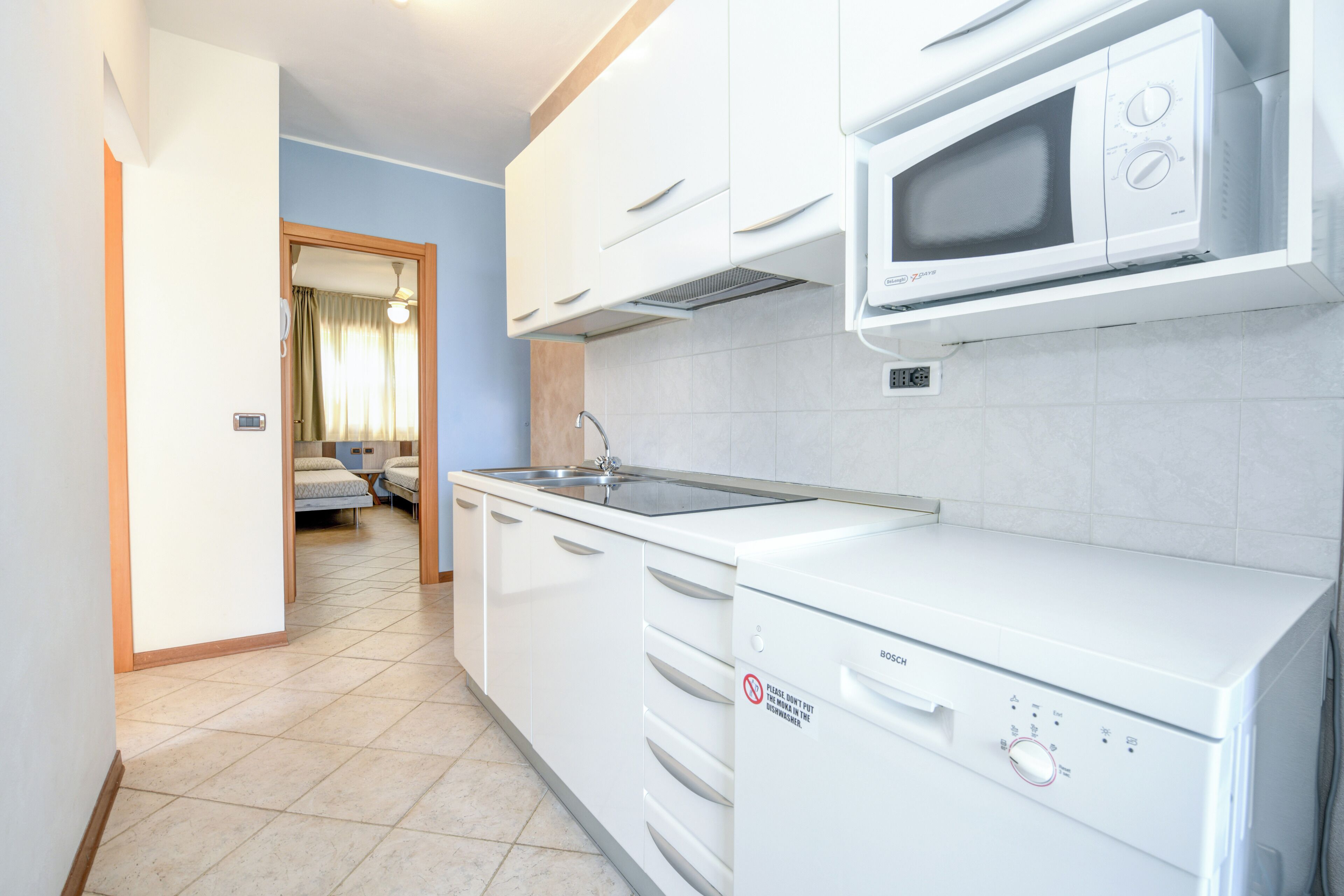 A modern kitchen with white appliances, a sink, and a window with curtains.