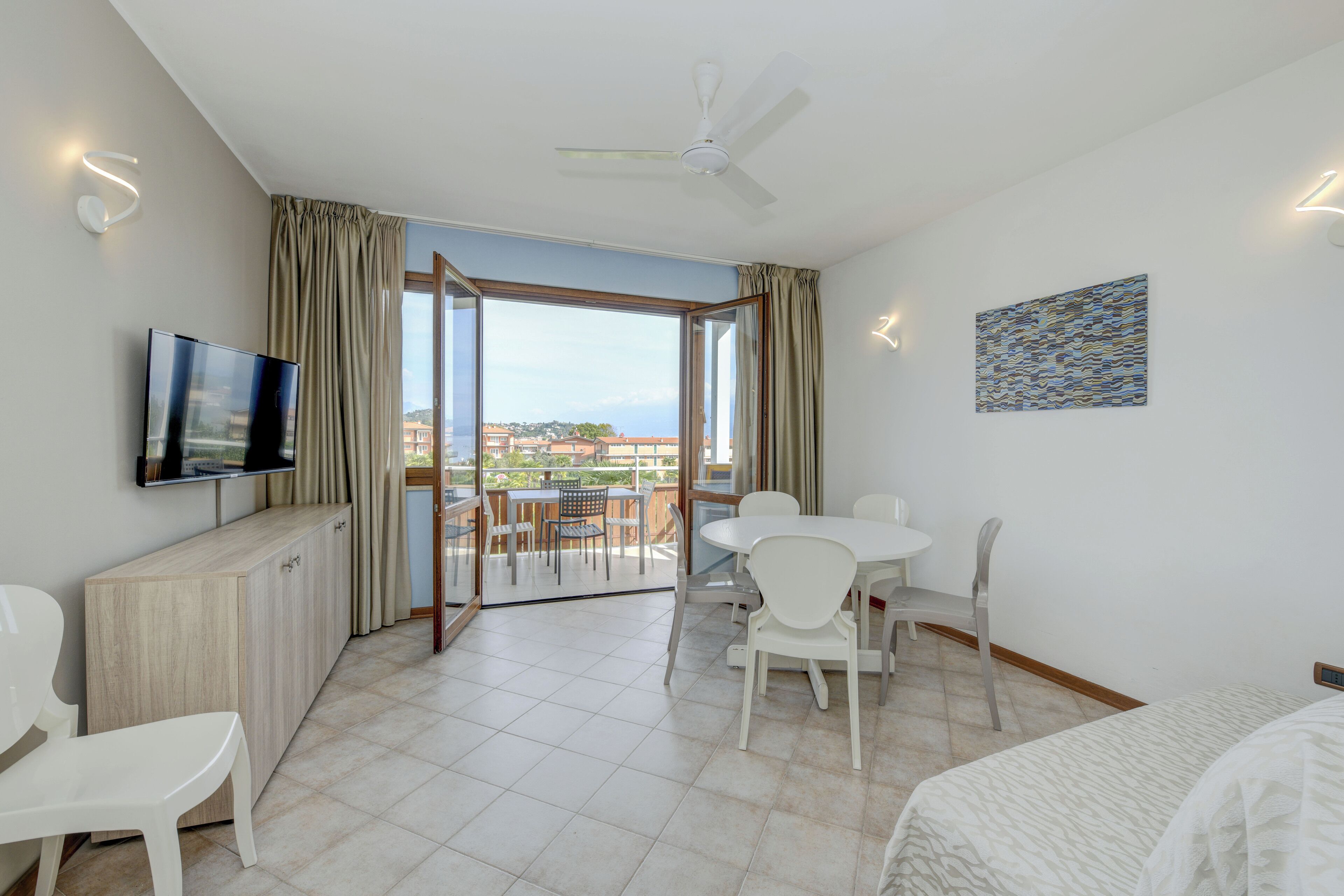 Une chambre d’hôtel avec balcon, un coin repas, une télévision et un ventilateur de plafond.