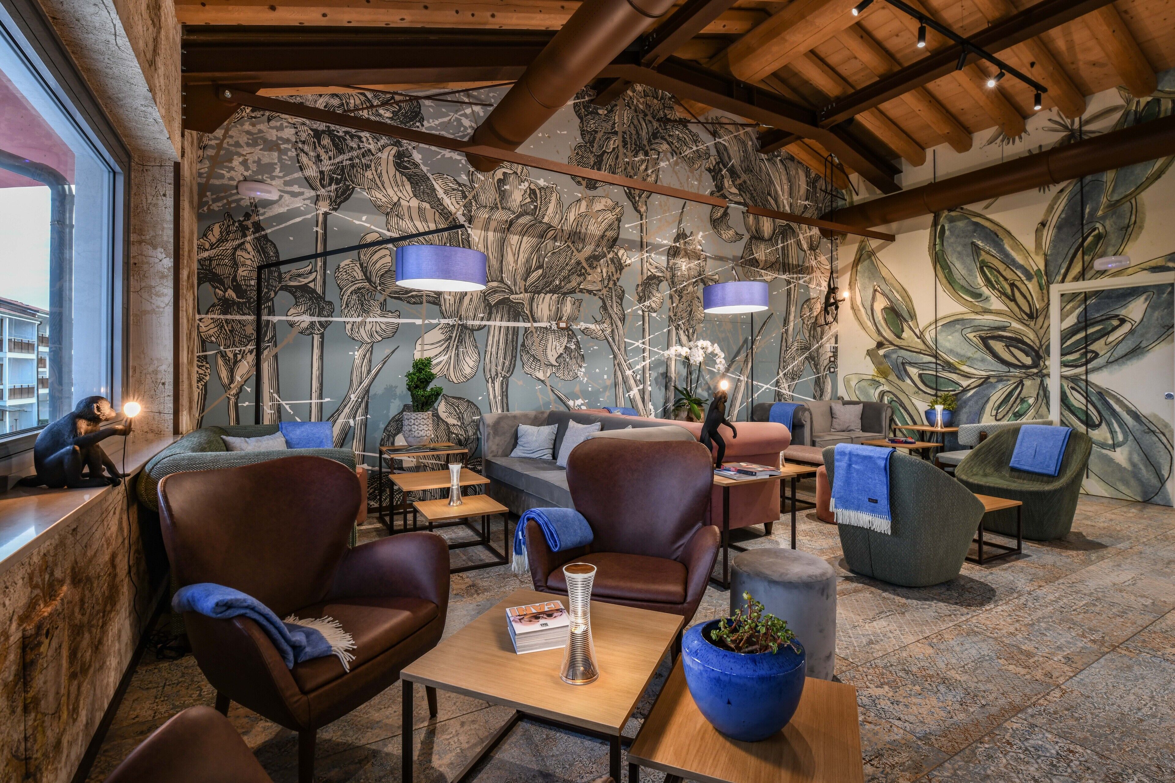 A modern lounge area with leather sofas, wooden tables, and a large mural of flowers on the wall.