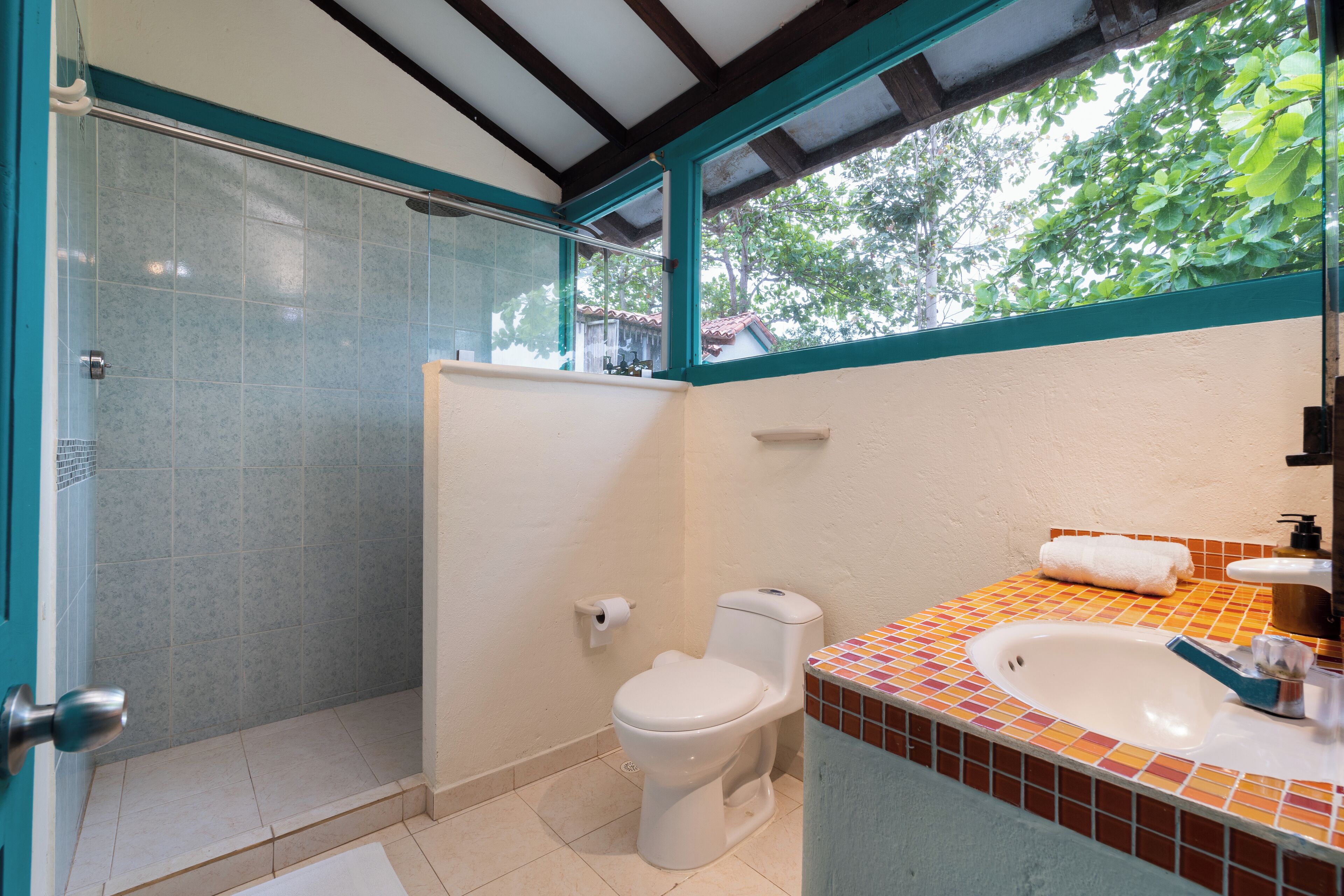 Ein Badezimmer mit Dusche, Toilette, Waschbecken und einem Fenster mit Blick auf Bäume.