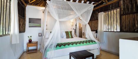 A room with a bed under a canopy, a wooden nightstand with a vase, and a small table.