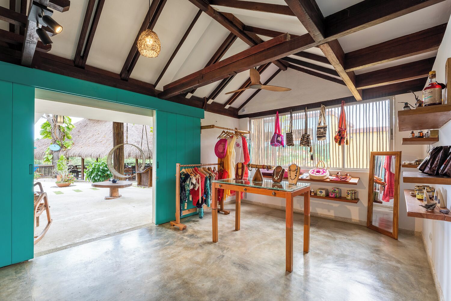L’intérieur d’un hôtel-boutique présente un plafond en bois, une table centrale sur laquelle sont suspendus divers objets, et une vue sur l’extérieur.