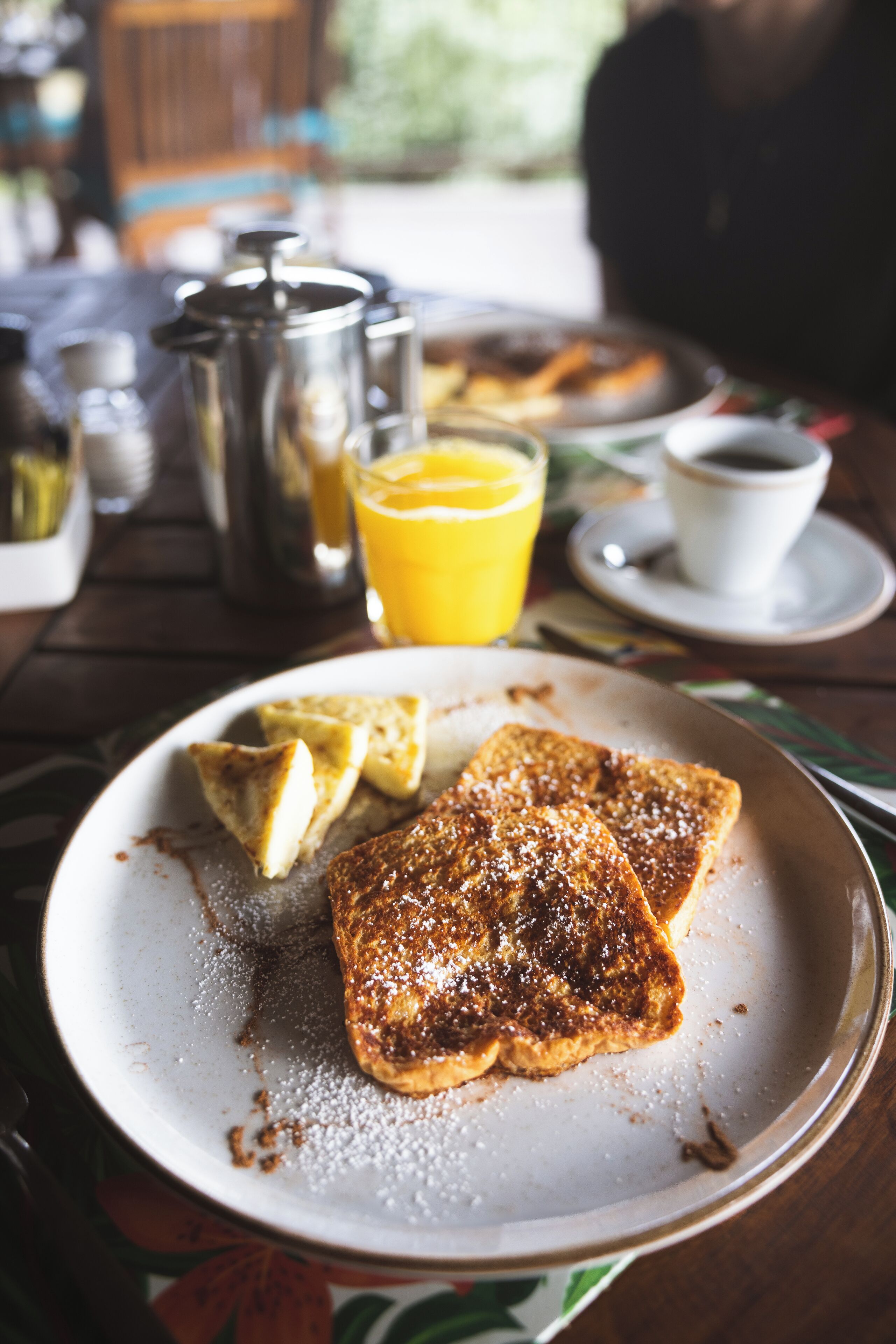Un desayuno con tostadas, una taza de café y un vaso de jugo de naranja sobre una mesa.