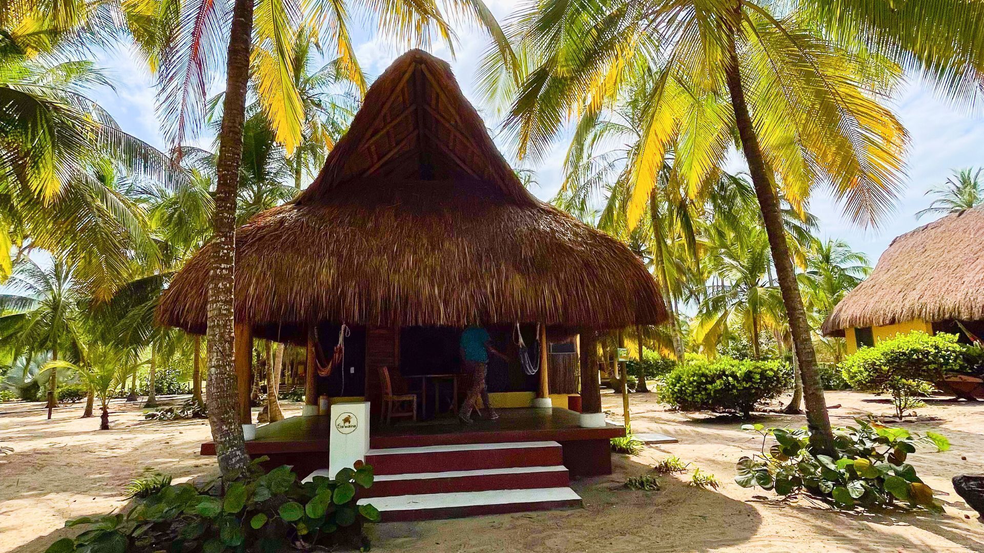A thatched-roof hut with a staircase leading up to it, surrounded by palm trees.