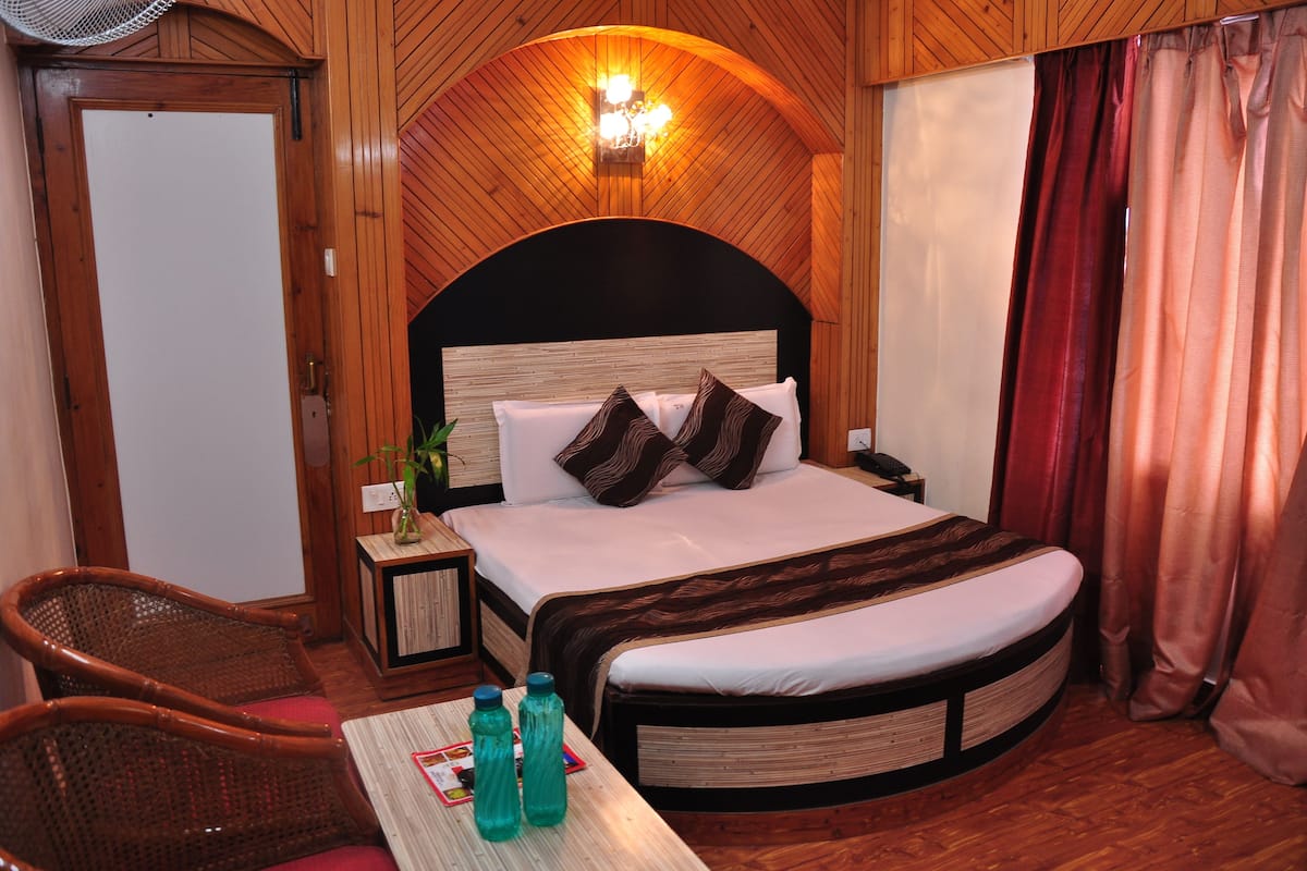A wooden-paneled room with a bed, a nightstand, a chair, and a table with water bottles.