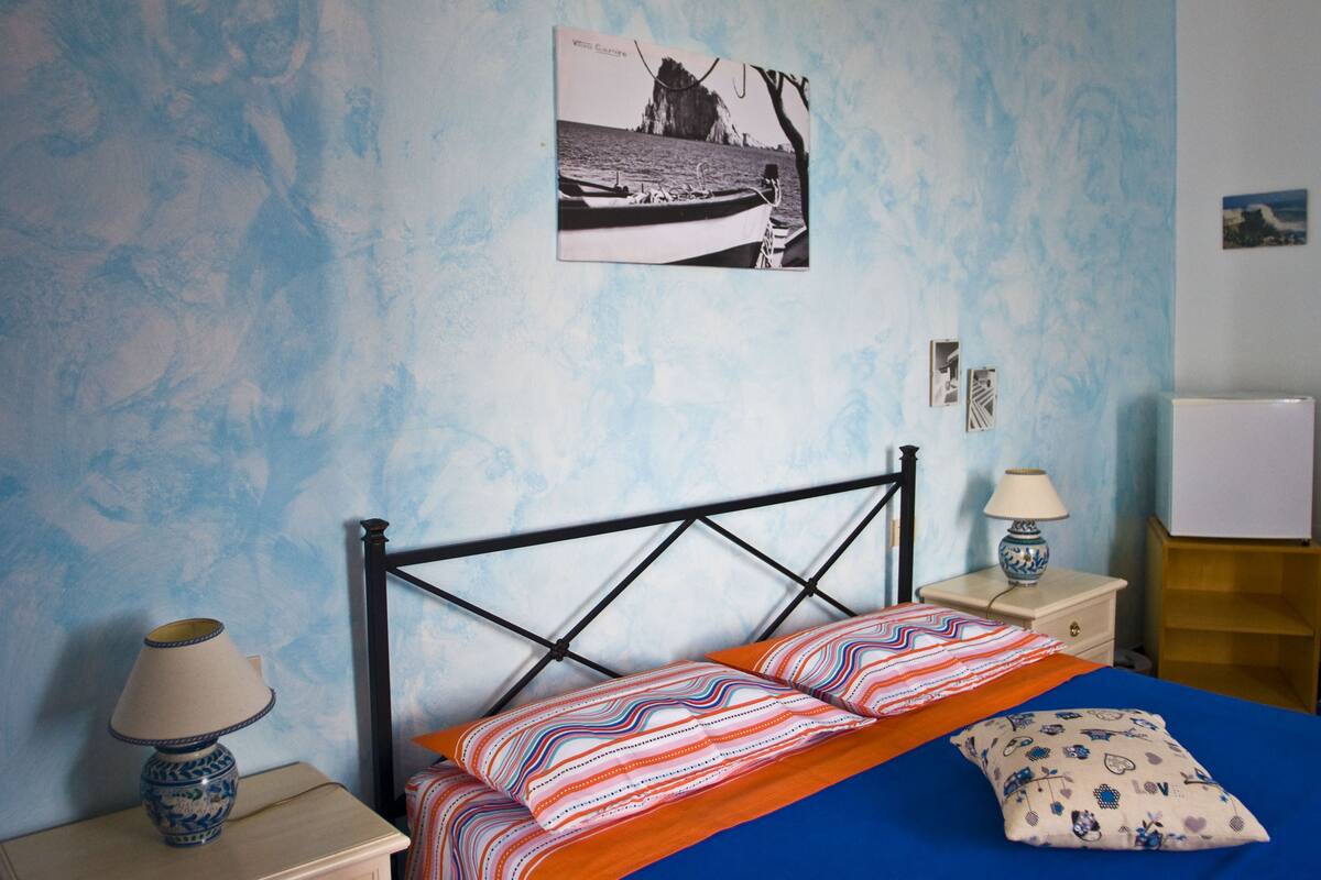 A bedroom with a bed, two bedside tables, a lamp, a wall-mounted picture, and a nightstand.
