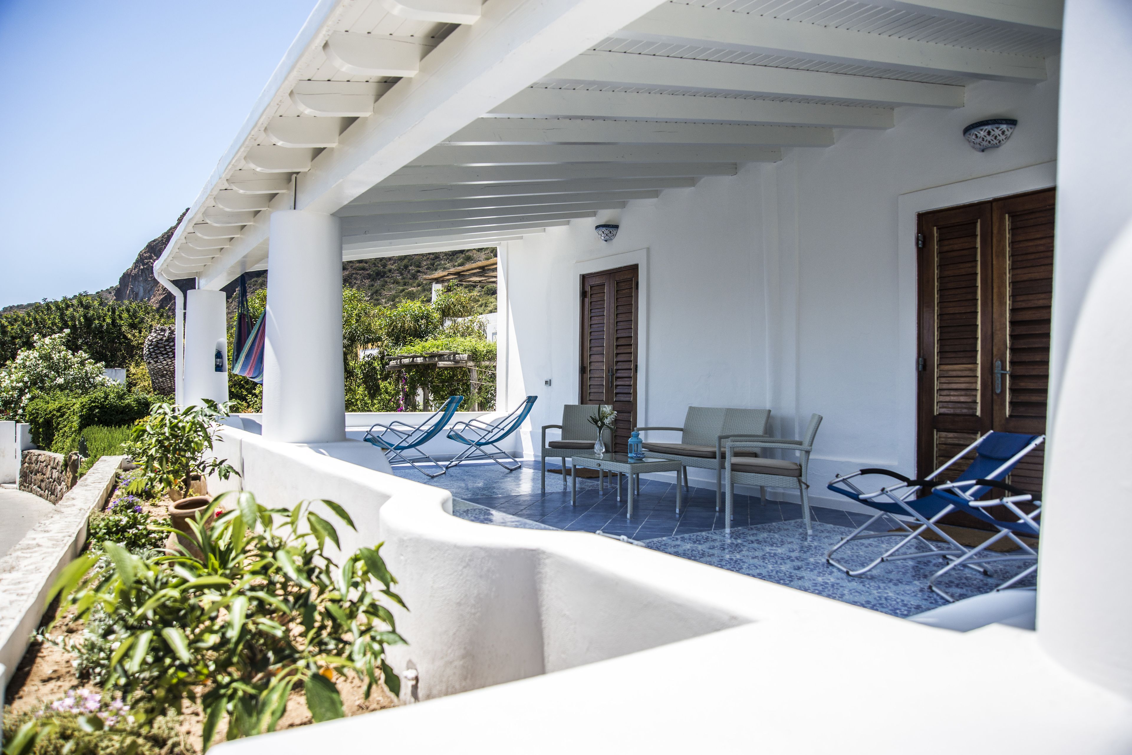 A covered outdoor area with white walls, blue lounge chairs, and a table.