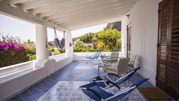 A covered outdoor area with blue patterned flooring, a table with chairs, and a hammock. - La Sirena (Lipari)