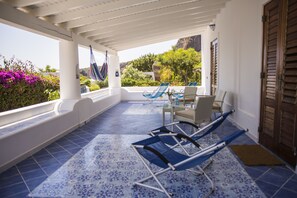 A covered outdoor area with blue patterned flooring, a table with chairs, and a hammock. - La Sirena (Lipari)