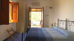 A bedroom with a bed, a wooden chair, a small table with a lamp, and an open door leading to a balcony. - La Sirena (Lipari)