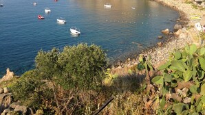 A coastal landscape with boats on calm waters, rocky cliffs, and sparse vegetation. - La Sirena (Lipari)
