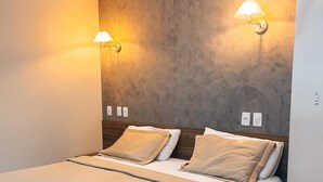 Una habitación de hotel moderna con una cama grande, dos lámparas fijadas a la pared y un revestimiento texturizado.