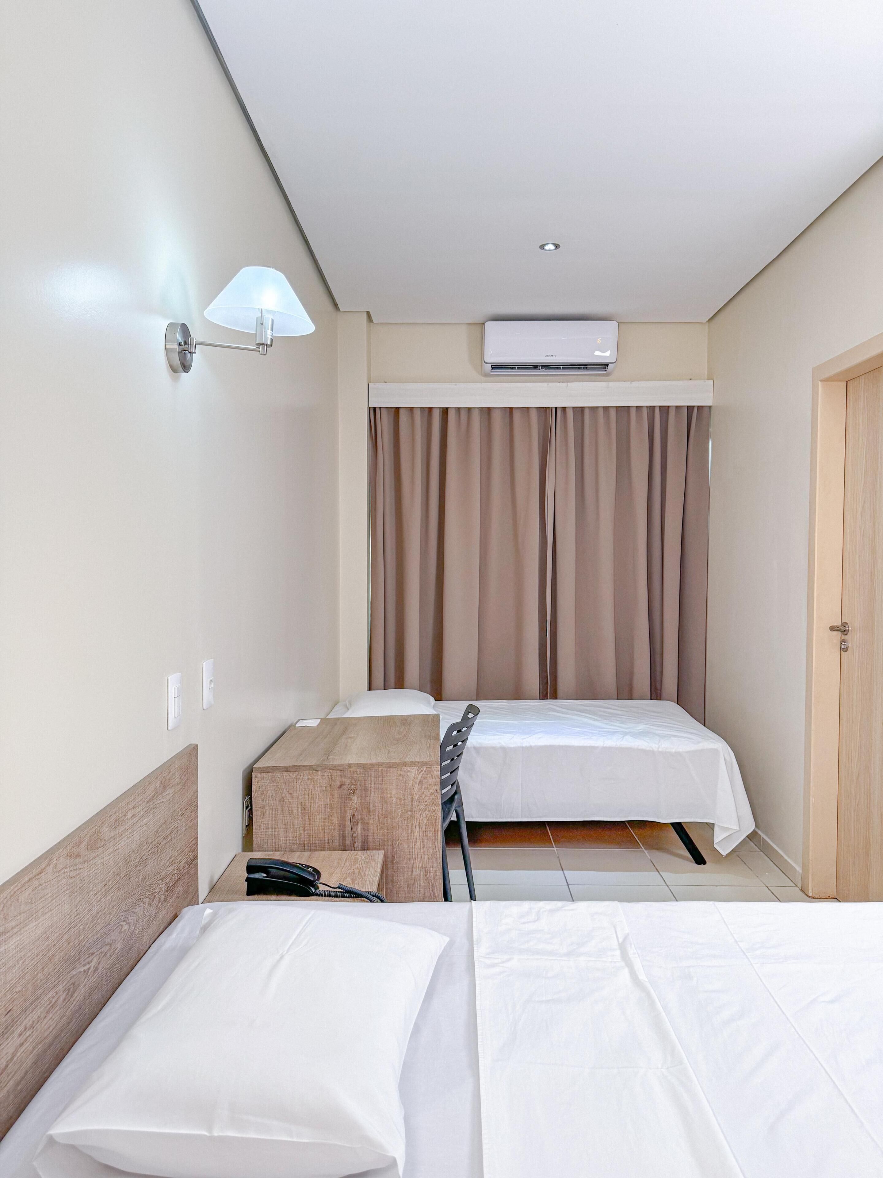 Une chambre d’hôtel avec deux lits, un climatiseur fixé au plafond, une lampe fixée au mur et une armoire en bois.