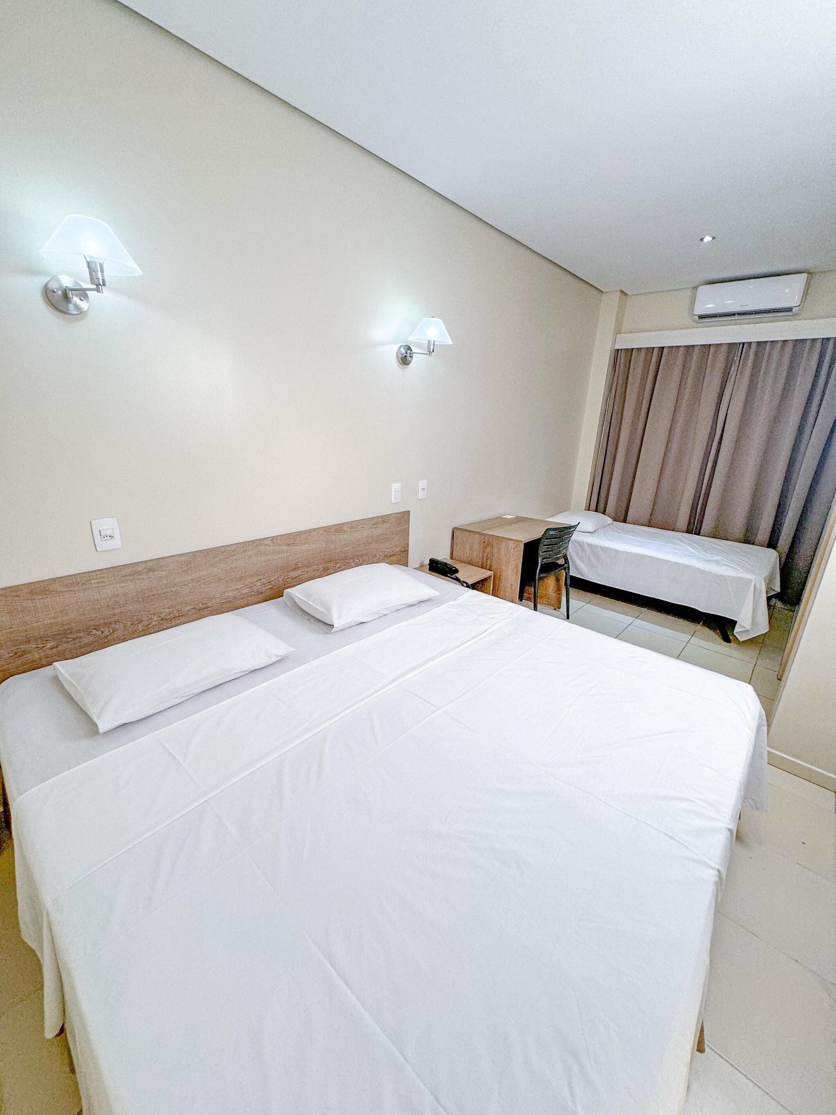 Habitación de hotel con una cama grande, una cama más pequeña, una mesita de noche, una lámpara y un equipo de aire acondicionado.