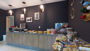 Mostrador de buffet con diversas opciones de comida y bebidas, un microondas y cuadros en la pared.