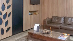 Una sala de estar moderna con un sofá de cuero marrón, un televisor de pantalla plana montado en una pared de madera, una mesa de centro con revistas y un estante pequeño con objetos decorativos.