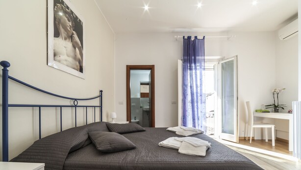 Une chambre à coucher avec un lit, un bureau, une chaise et une salle de bain visible à travers une porte ouverte.