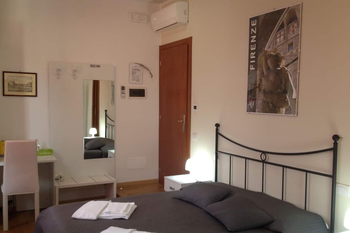 Een slaapkamer met een bed, een stoel, een bureau en een poster aan de muur.