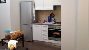 Une cuisine compacte équipée d’un réfrigérateur, d’une cuisinière et d’un four. On y trouve une petite table avec un panier de bananes et un récipient rempli de céréales.
