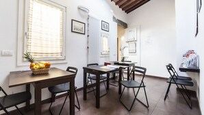 Un coin repas avec une table en bois, des chaises noires et un panier de fruits.