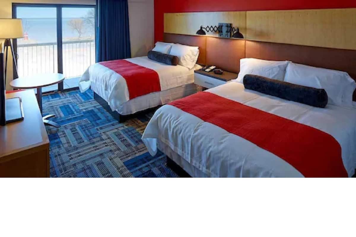 A hotel room with two beds, a desk, a chair, and a window with a view.