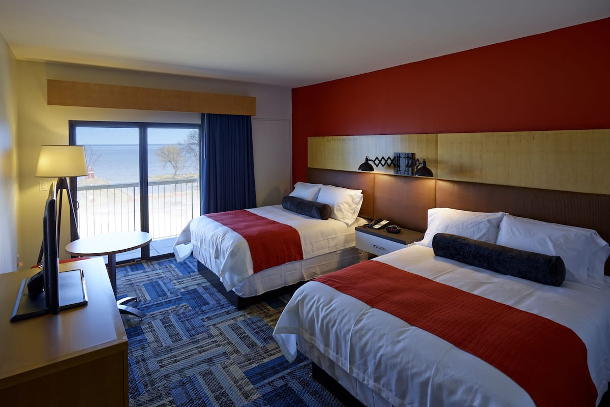 A hotel room with two beds, a desk, a lamp, and a view of the sea.