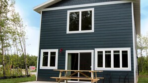 A two-story house with dark siding and white trim, featuring large windows and a front porch with a picnic table. - Eddy's Resort (Onamia)