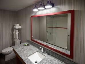 A bathroom with a large mirror, a sink, a toilet, and a shower.
