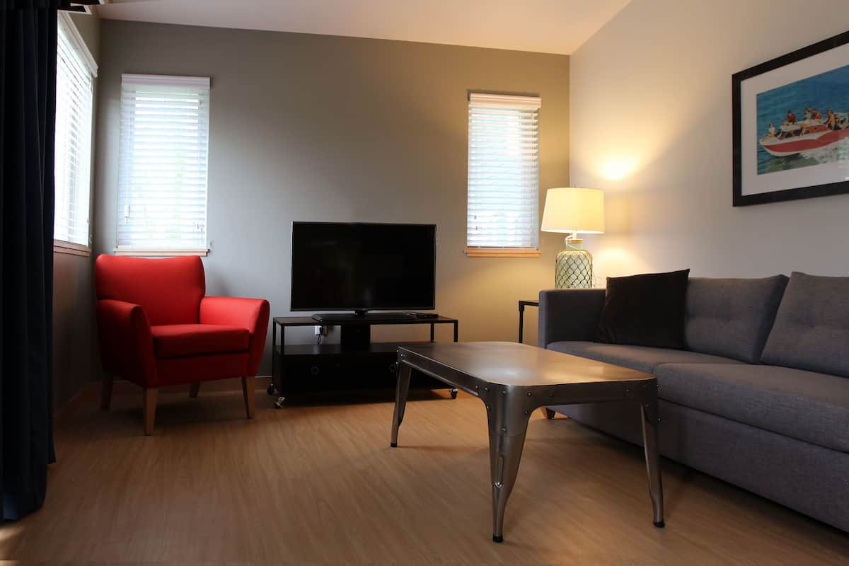 A modern living room with a red chair, grey sofa, a TV on a stand, and a lamp on a side table.