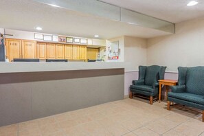 Zona de recepción con mostrador, armarios de madera, tablón de anuncios y dos sillones.