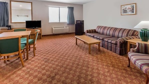 A hotel room with a dining table, chairs, a sofa, a TV, a heater, and a window with curtains. - Super 8 by Wyndham St. Charles (SAINT CHARLES)