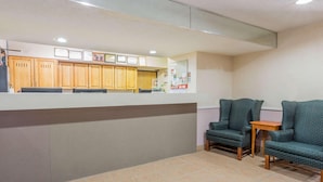 A reception area with a counter, wooden cabinets, two green armchairs, and a small wooden table. - Super 8 by Wyndham St. Charles (SAINT CHARLES)