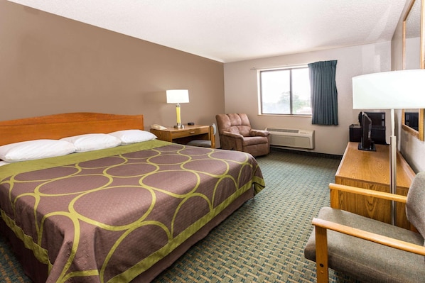 A hotel room with a large bed, a desk with a lamp, a chair, a TV, and a window with curtains.