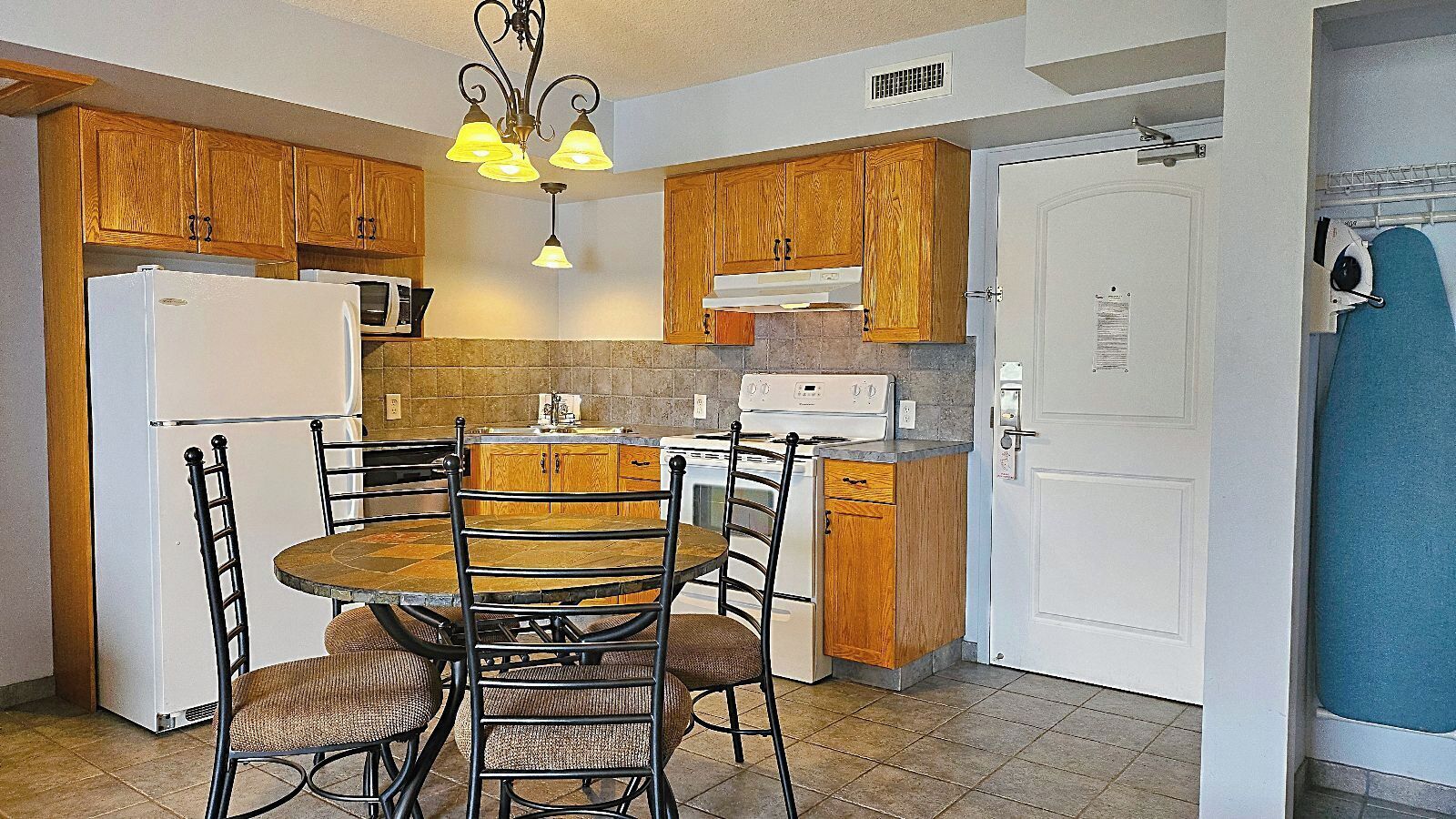 Una cocina con armarios de madera, un refrigerador blanco, una estufa y una mesa de comedor con sillas.